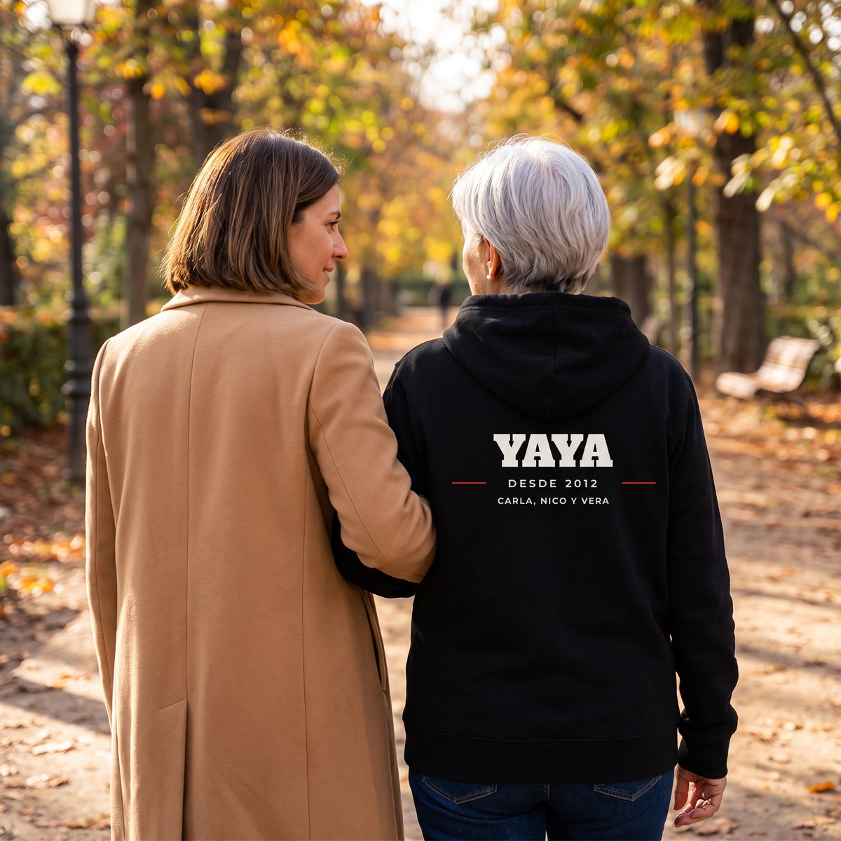 Abuela de espaldas paseando con su hija con la sudadera con capucha negra personalizada con YAYA, DESDE 2012 y los nombres de sus nietos, estampado en la espalda