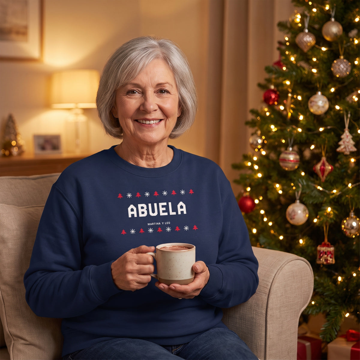 Abuela junto al árbol de Navidad con la sudadera azul marino personalizada con ABUELA en estilo jersey de punto navideño y los nombres de sus nietos