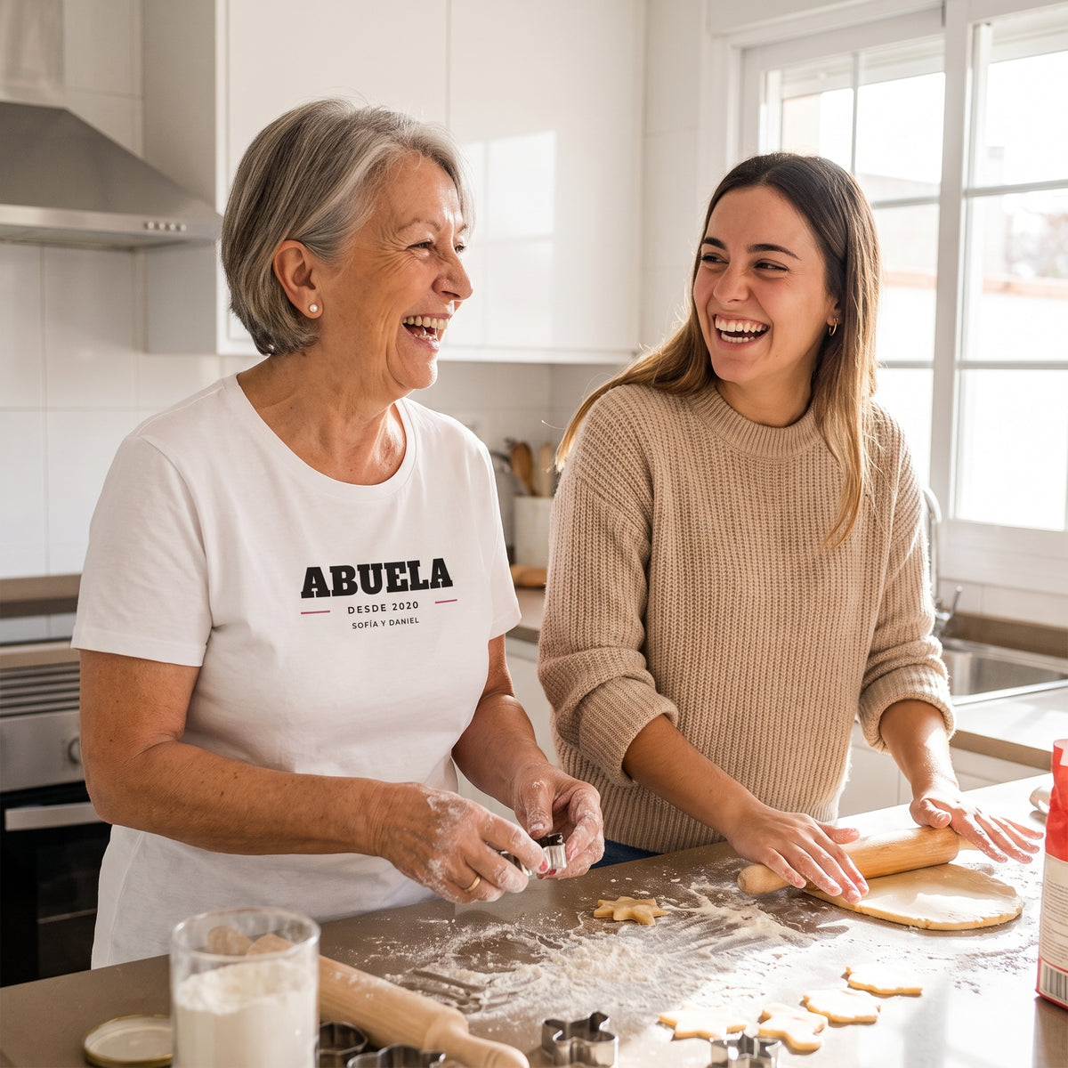 Abuela y nieta haciendo galletas de Navidad; la abuela lleva la camiseta blanca personalizada con ABUELA, DESDE 2020 y los nombres de sus nietos