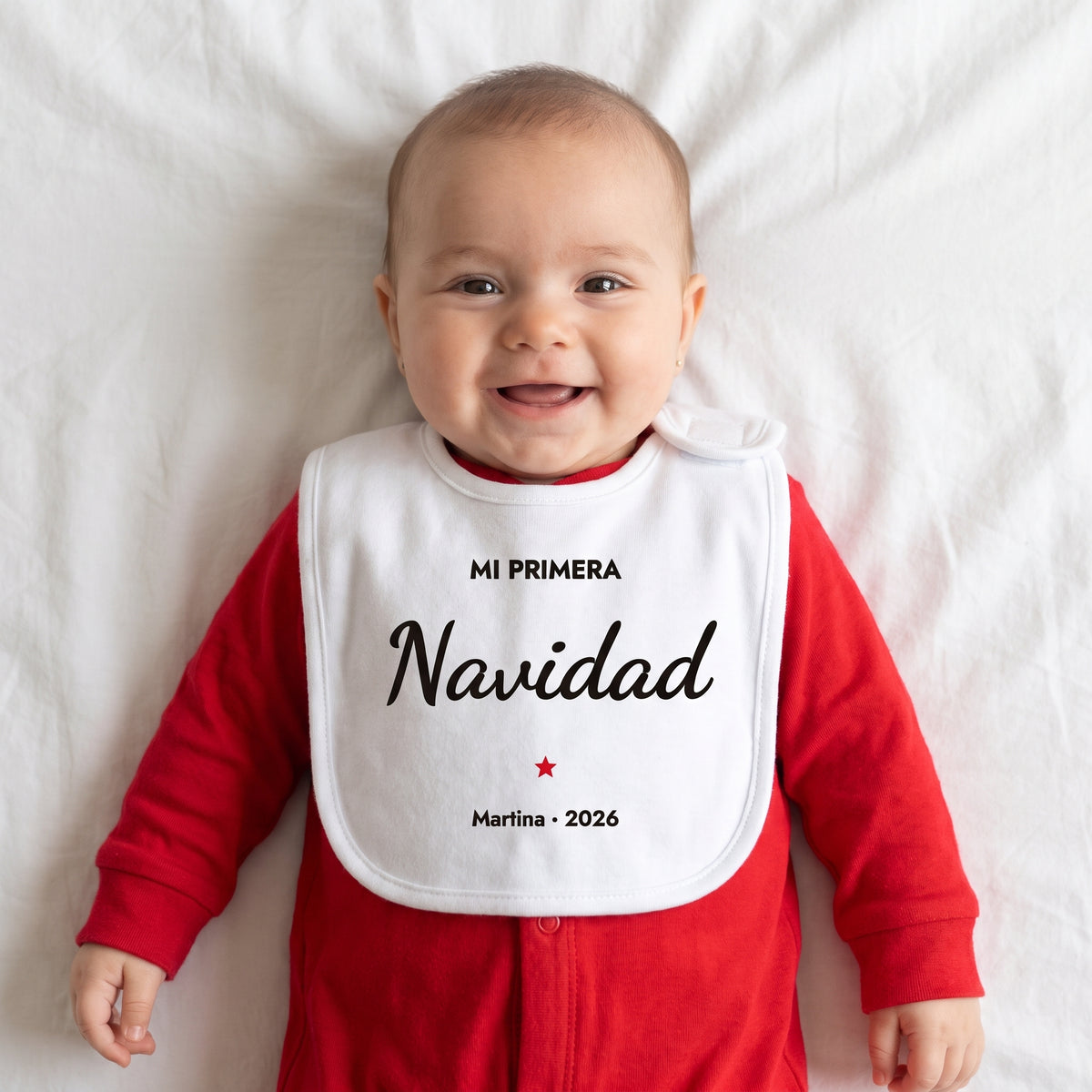 Bebé con pijama rojo y babero personalizado de su primera Navidad