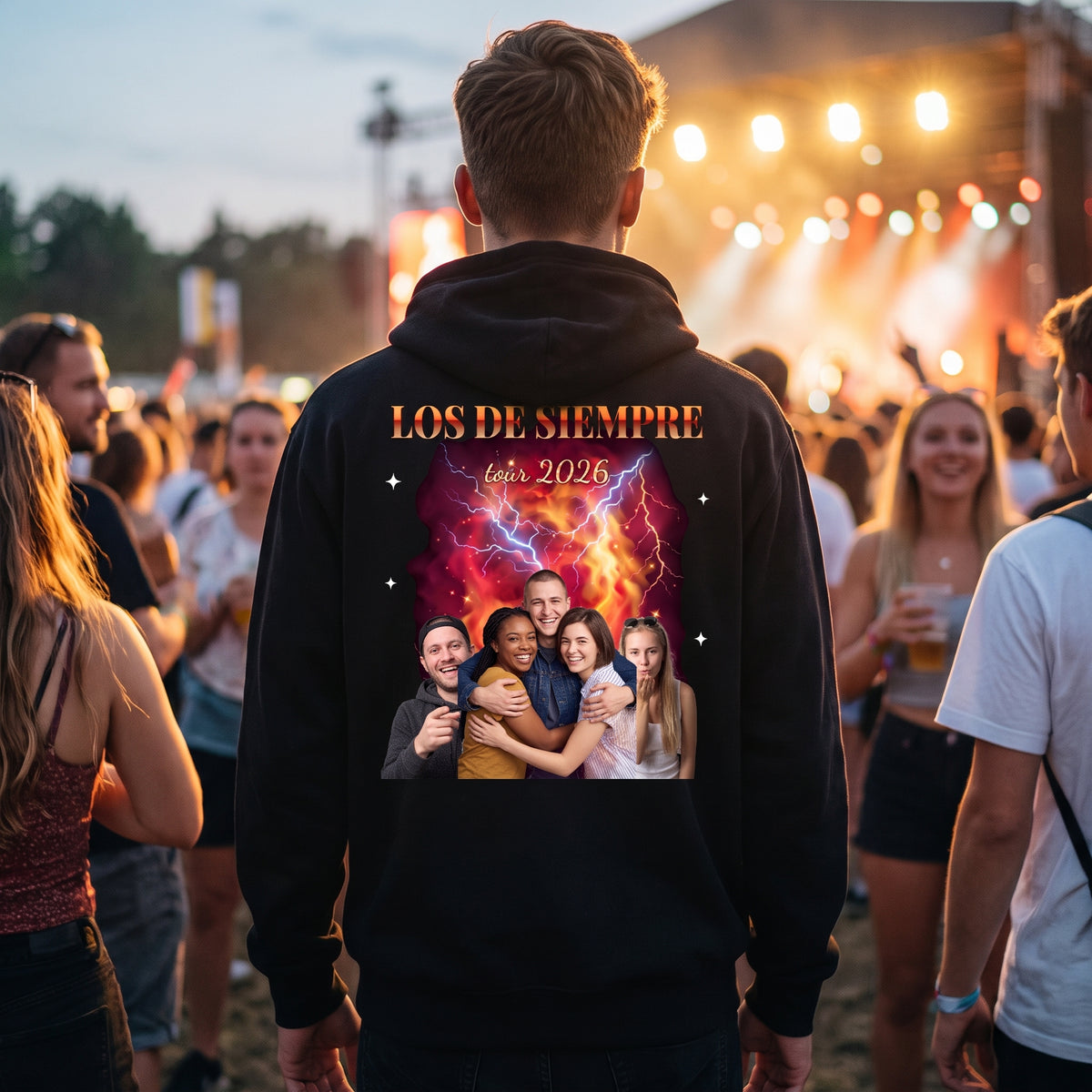 Chico de espaldas en un festival de música con la sudadera con capucha negra personalizada estilo bootleg, fotos de sus amigos sobre fuego y rayos y «LOS DE SIEMPRE», estampada en la espalda