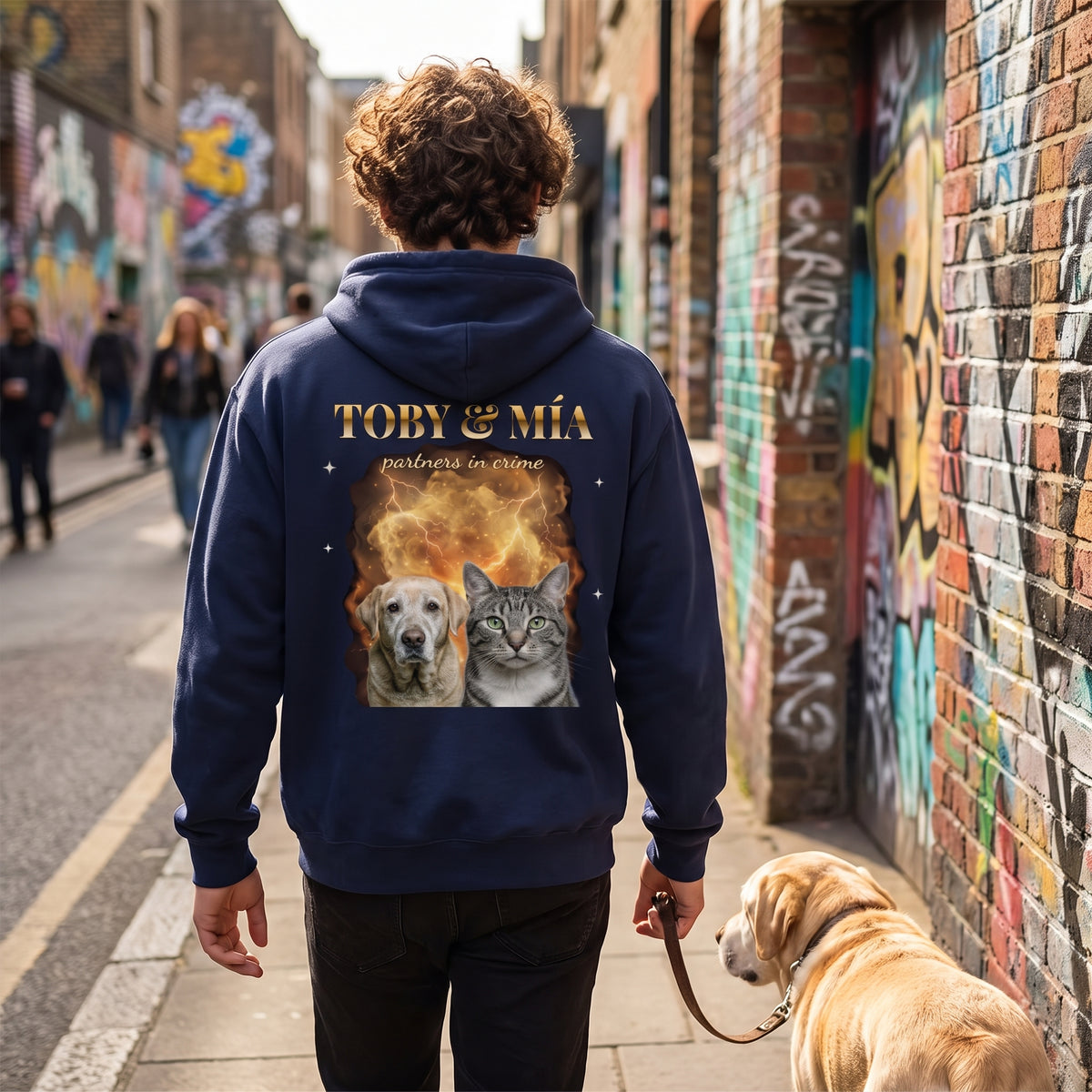 Chico de espaldas paseando a su labrador por una calle con grafitis, con una sudadera con capucha azul marino estilo bootleg con su perro y su gato, TOBY & MÍA y «partners in crime» en la espalda