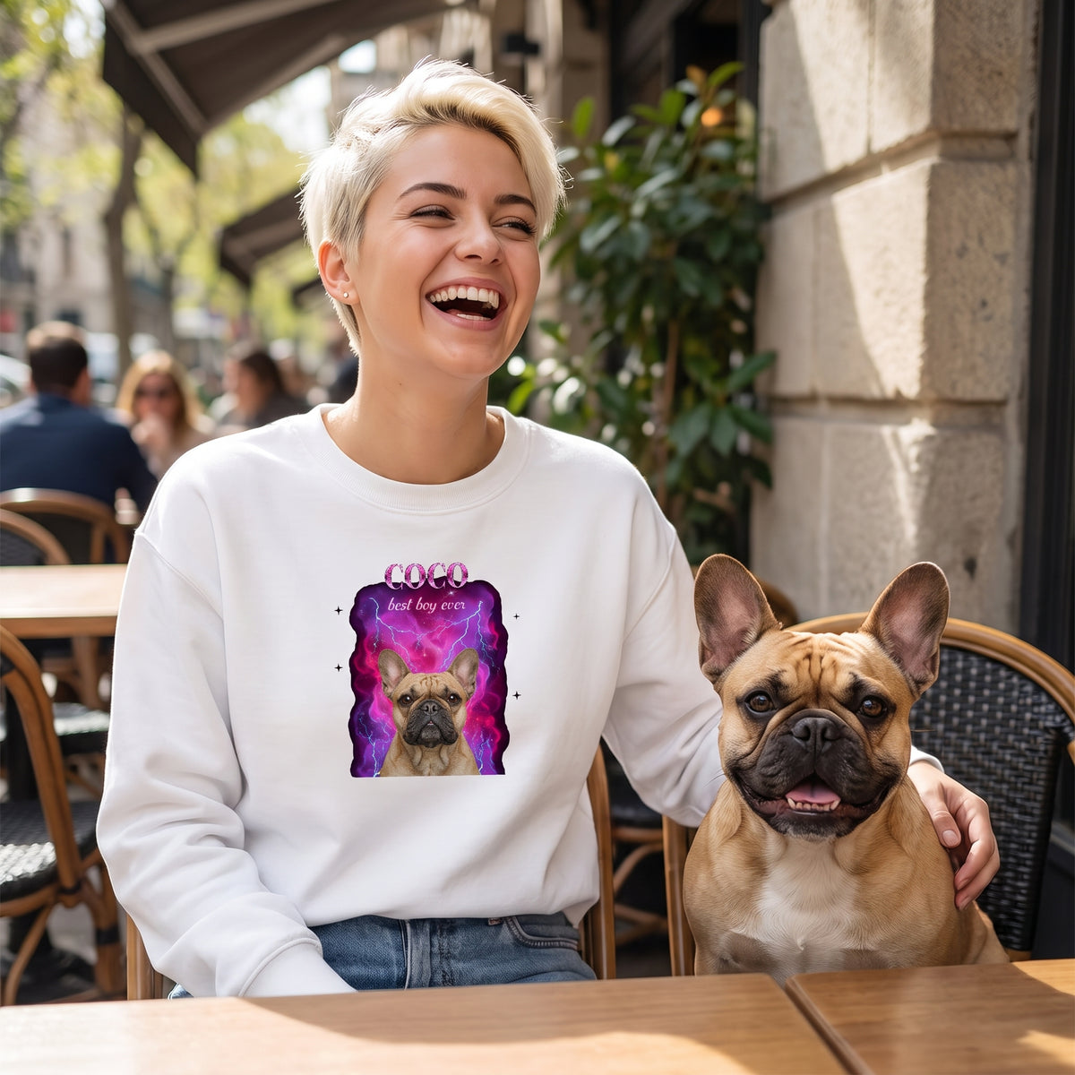 Chica riendo en una terraza junto a su bulldog francés, con una sudadera blanca estilo bootleg con la foto del perro sobre humo y rayos rosas, COCO y «best boy ever»