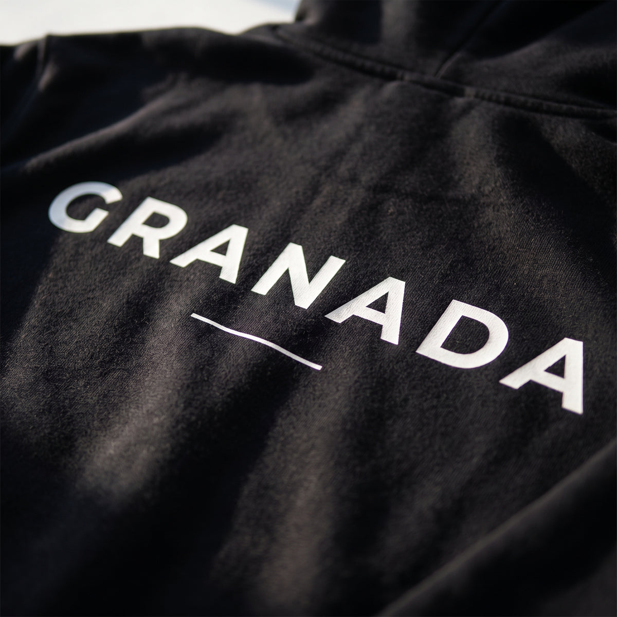 Detalle del estampado DTF de Granada y sus coordenadas sobre el tejido de una sudadera con capucha negra