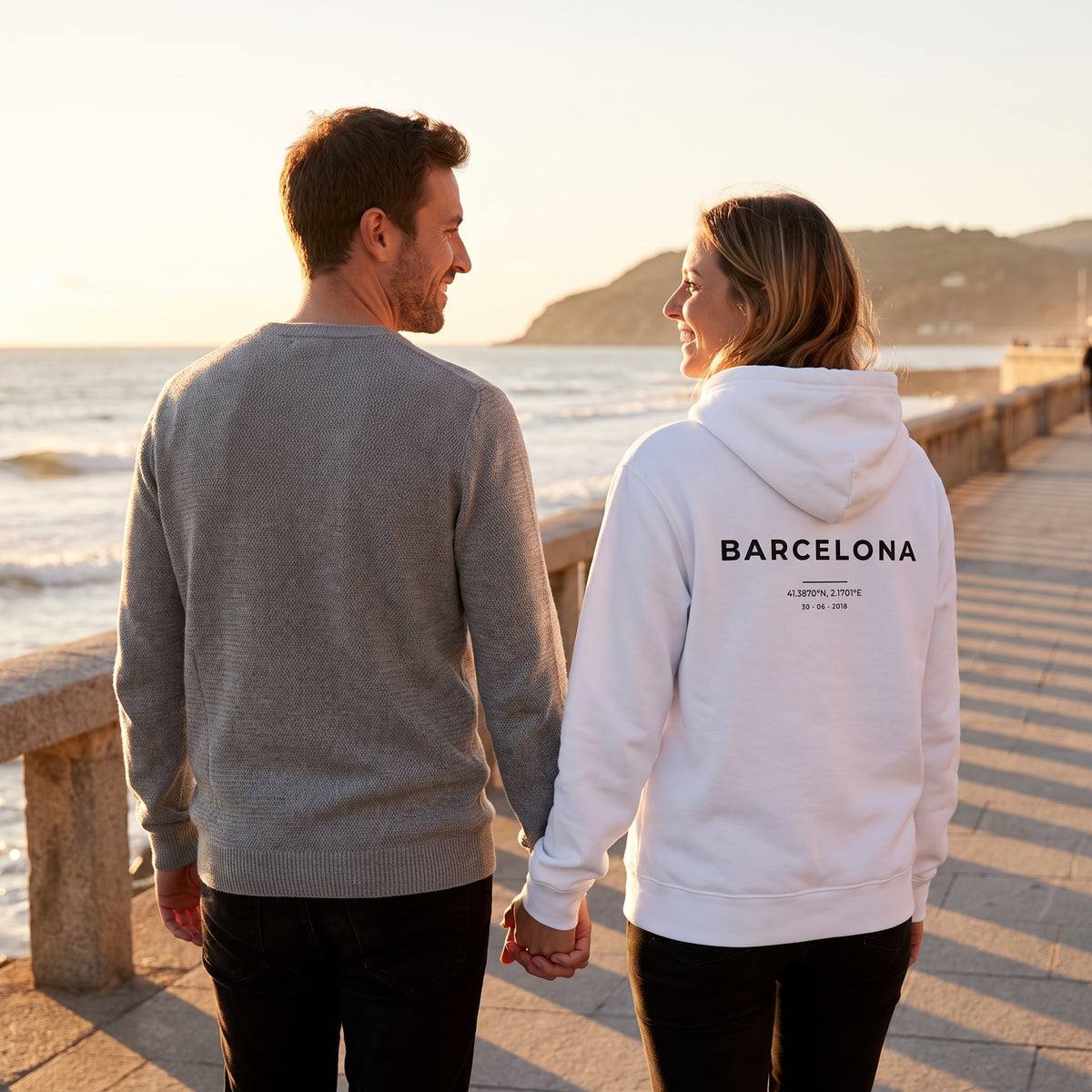 Paseo al atardecer con la sudadera con capucha blanca personalizada con Barcelona y sus coordenadas estampado en la espalda