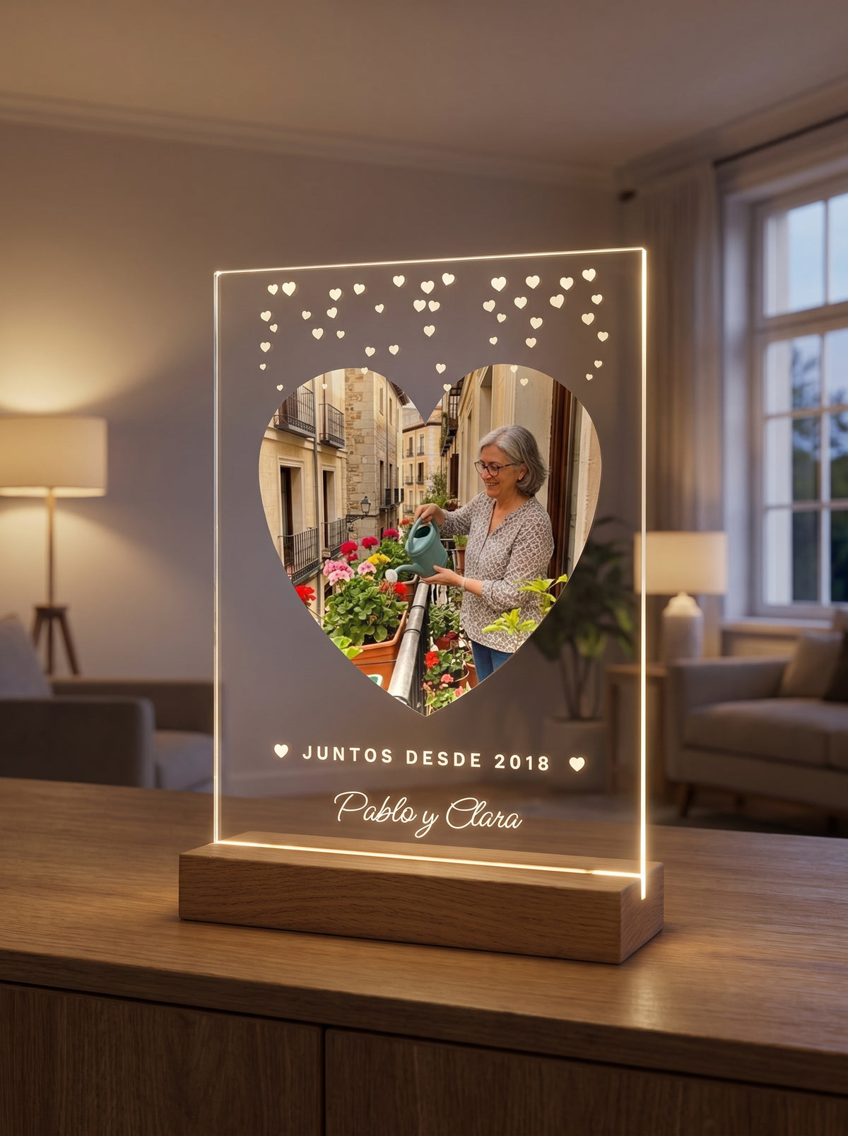 Placa de metacrilato personalizada con corazoncitos encendida sobre su base de roble con luz LED, en un salón al atardecer