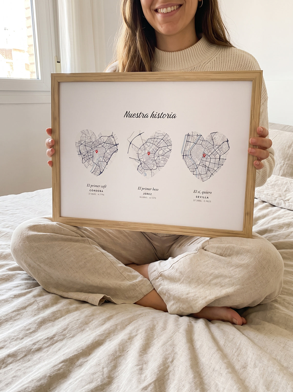 Una mujer sostiene sobre la cama el cuadro con tres mapas en forma de corazón de Córdoba, Jerez y Sevilla