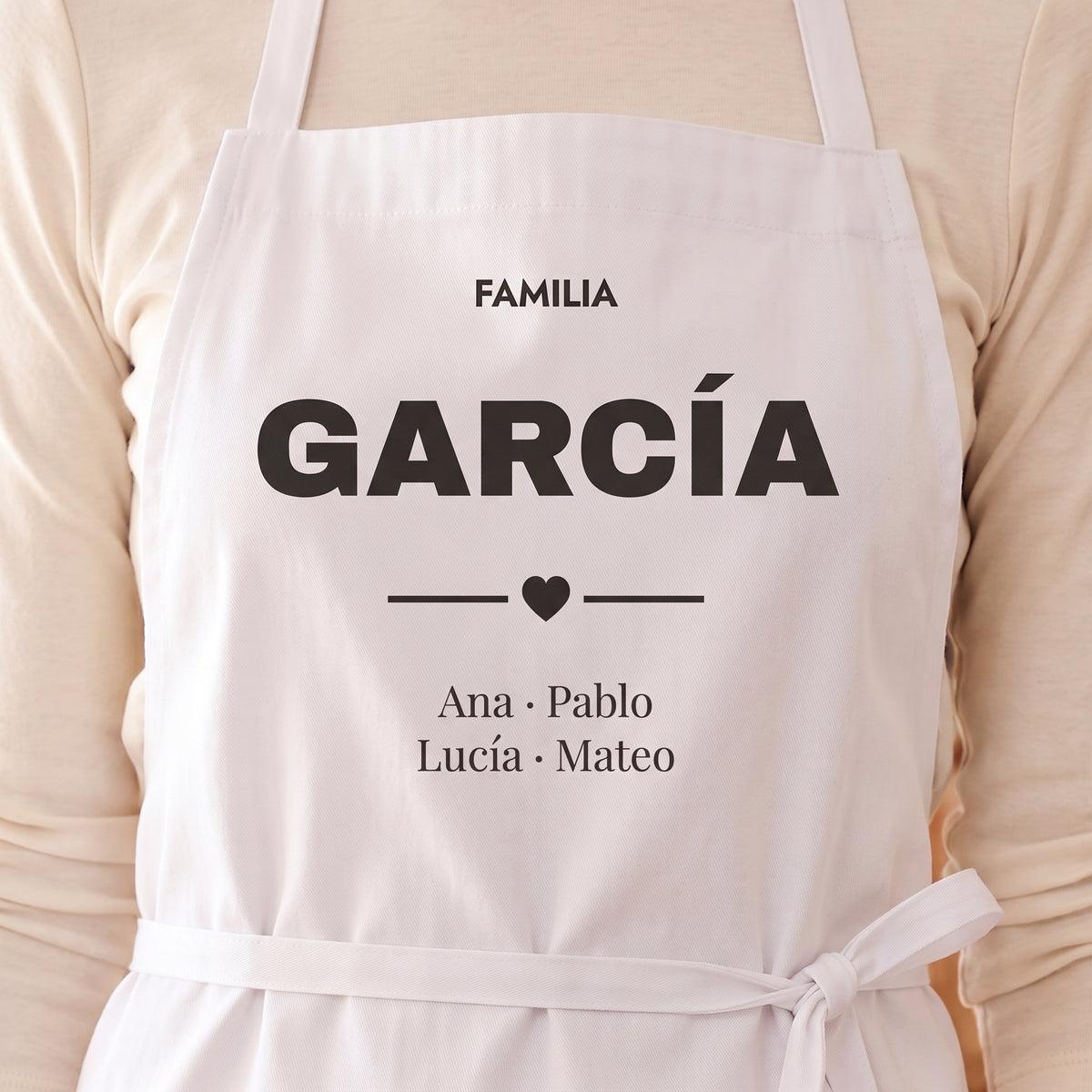 Detalle del peto de un delantal con «FAMILIA GARCÍA», un corazón y los nombres Ana, Pablo, Lucía y Mateo