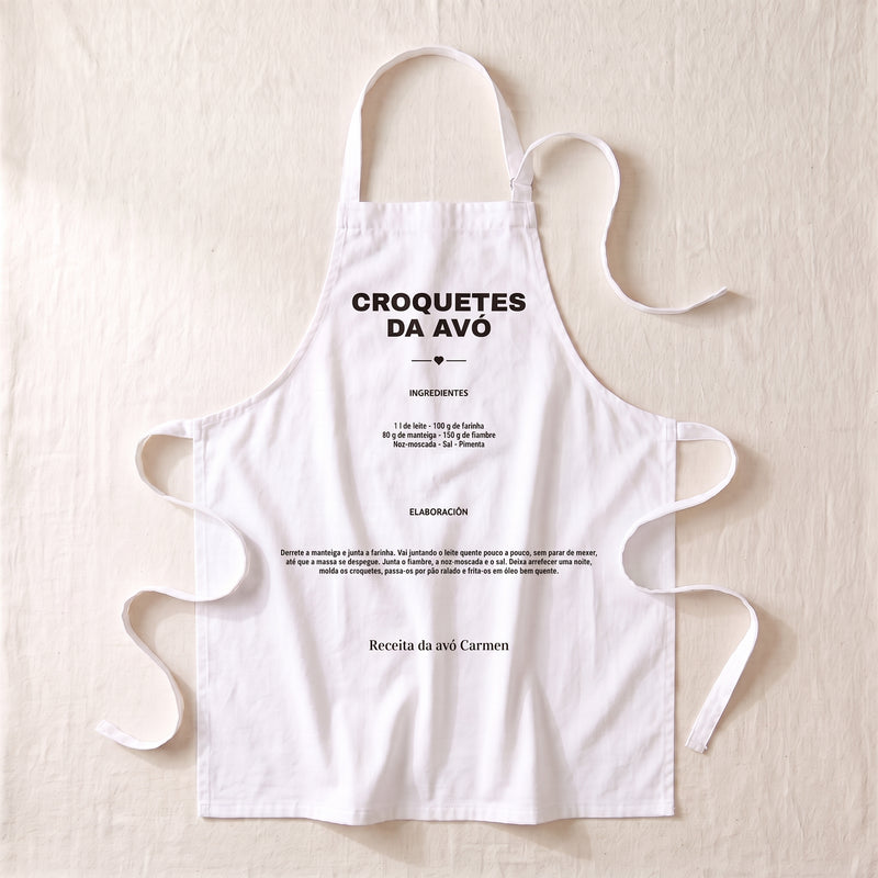 Delantal personalizado blanco extendido, con la receta de las croquetas de la abuela impresa en el peto: el nombre del plato, los ingredientes, la elaboración y la firma «Receta de la abuela Carmen»