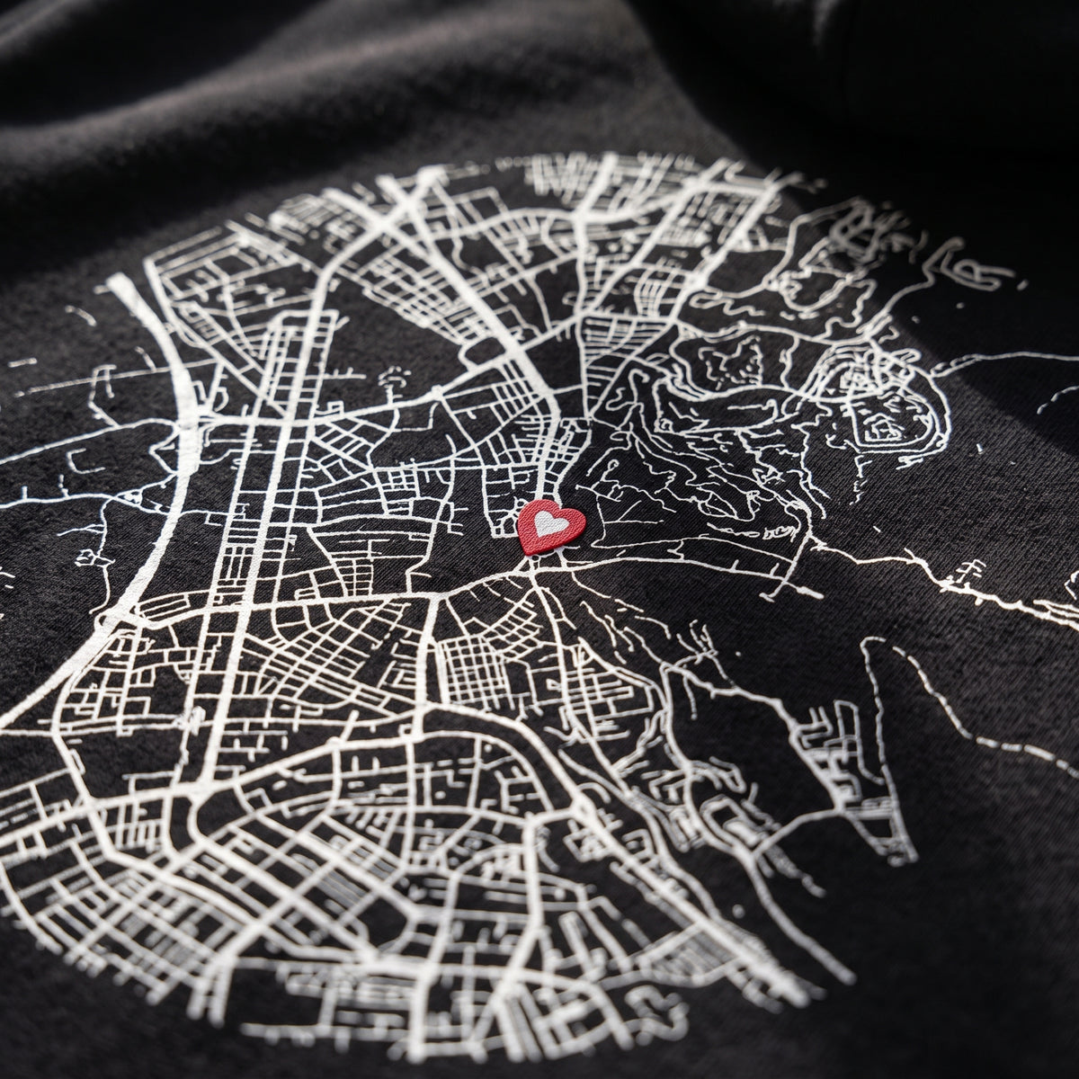 Detalle del estampado DTF del mapa de Granada y «Nuestro primer café» sobre el tejido de una sudadera con capucha negra