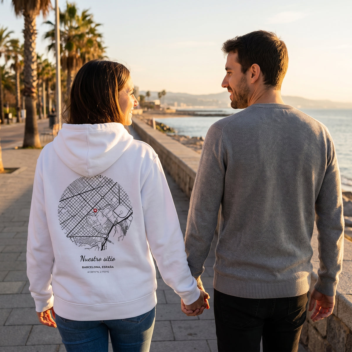 Paseo al atardecer con la sudadera con capucha blanca personalizada con el mapa de Barcelona y «Nuestro sitio» estampado en la espalda