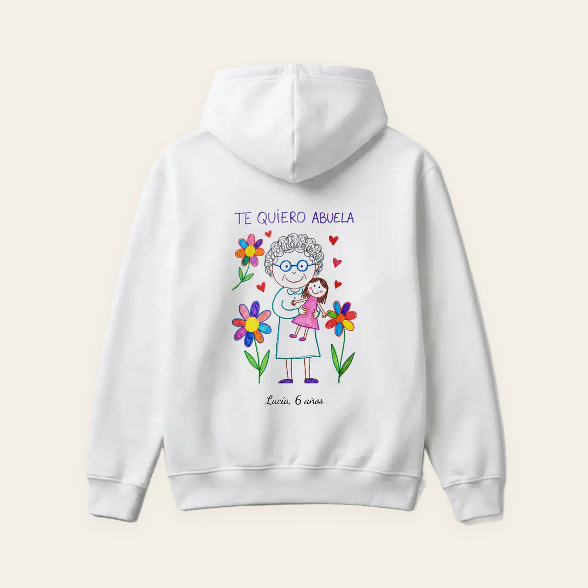 Sudadera con capucha blanca personalizada con el dibujo de una nieta —su abuela con gafas entre flores y «TE QUIERO ABUELA»— y «Lucía, 6 años», estampado en la espalda con sus colores