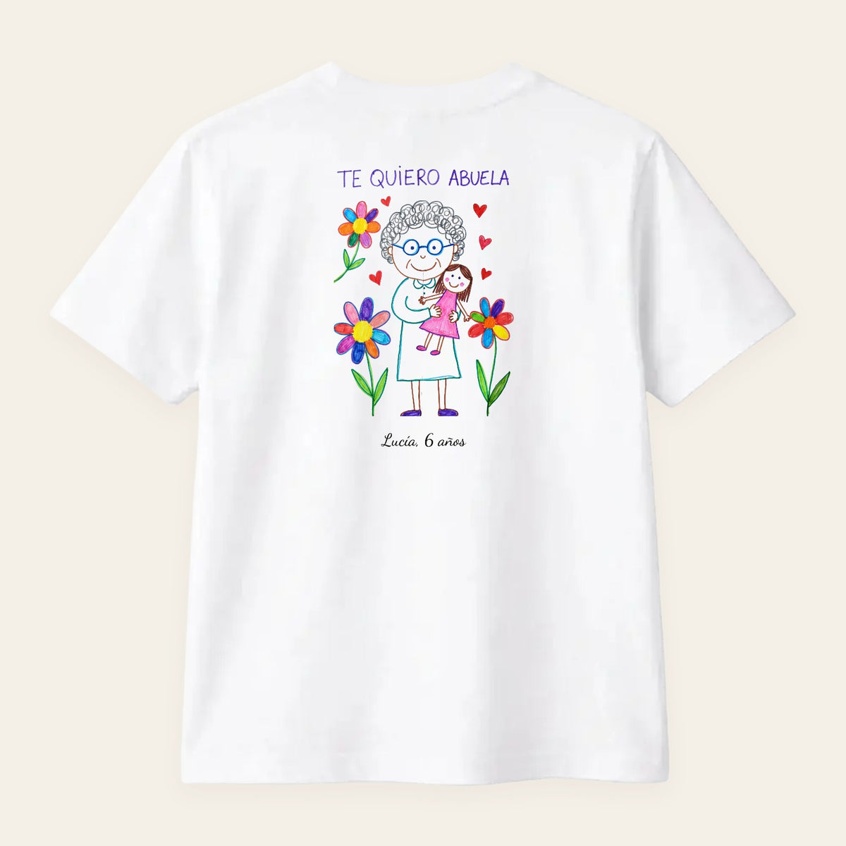 Camiseta blanca personalizada con el dibujo de su nieta —su abuela con flores y «TE QUIERO ABUELA»— y «Lucía, 6 años», estampado en la espalda