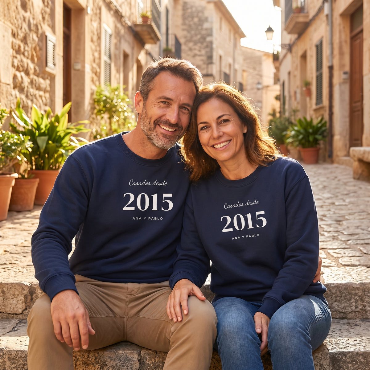 Pareja sentada en una calle del casco antiguo con sus sudaderas azul marino iguales «Casados desde 2015», Ana y Pablo