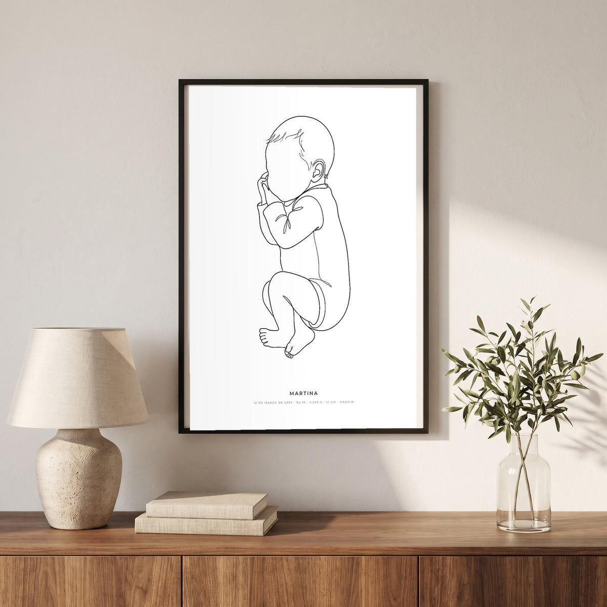 Cuadro personalizado de bebé en dibujo lineal minimalista, en marco negro sobre un aparador de nogal