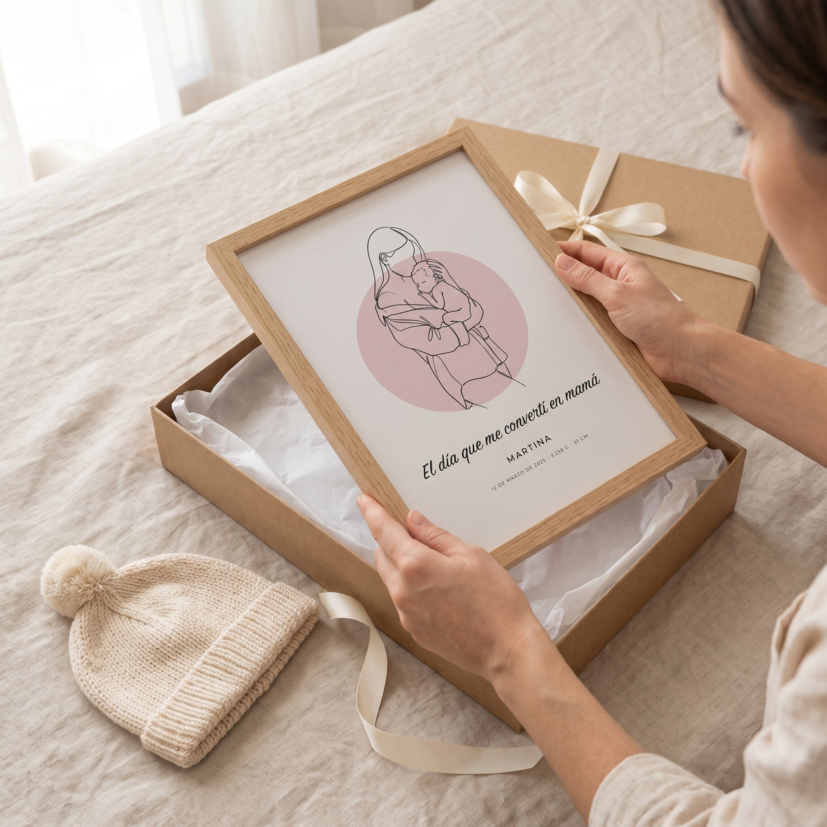 Una madre saca de su caja de regalo el cuadro de dibujo lineal con su bebé y la frase «El día que me convertí en mamá»