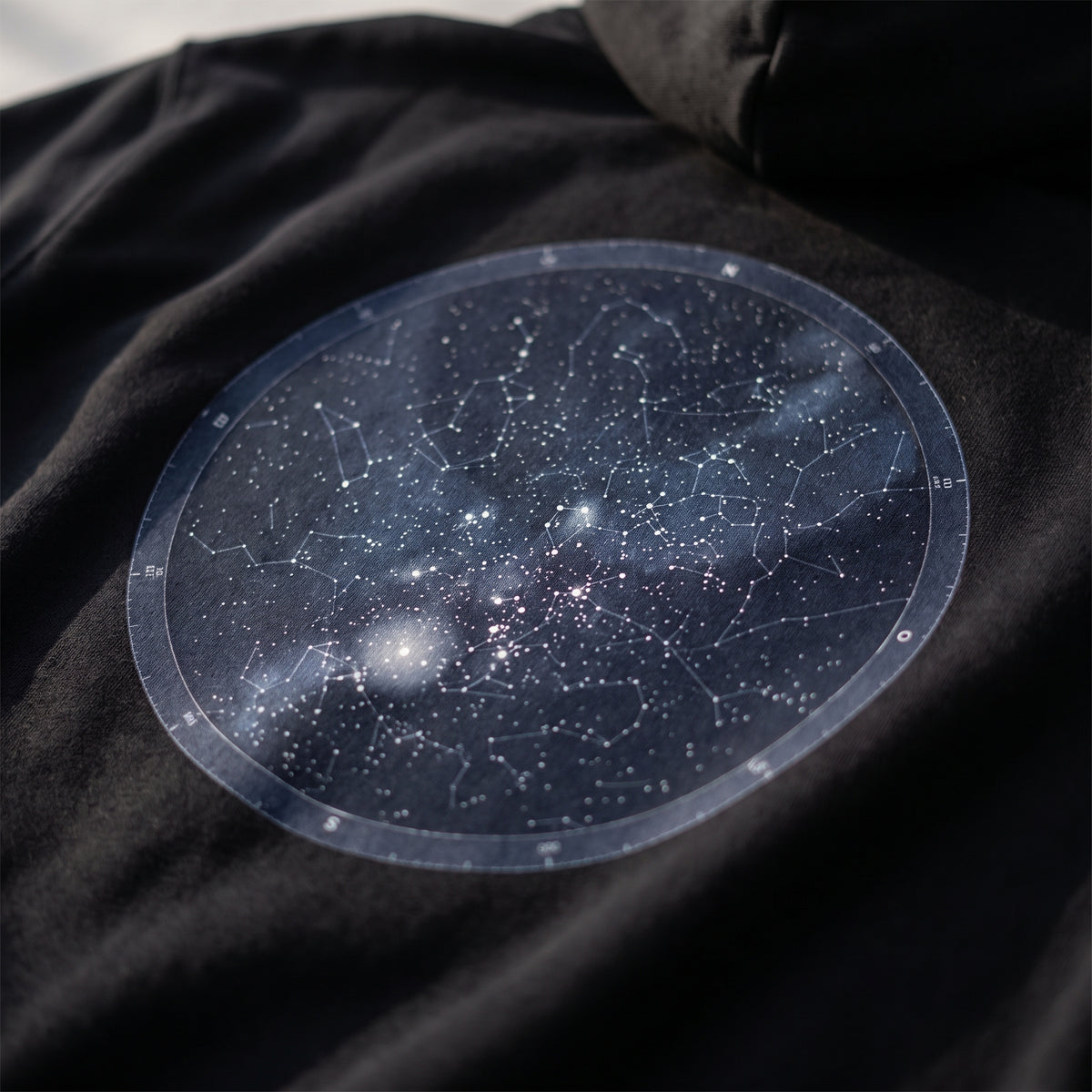 Detalle del estampado DTF del mapa estelar del cielo de Granada sobre el tejido de una sudadera con capucha negra