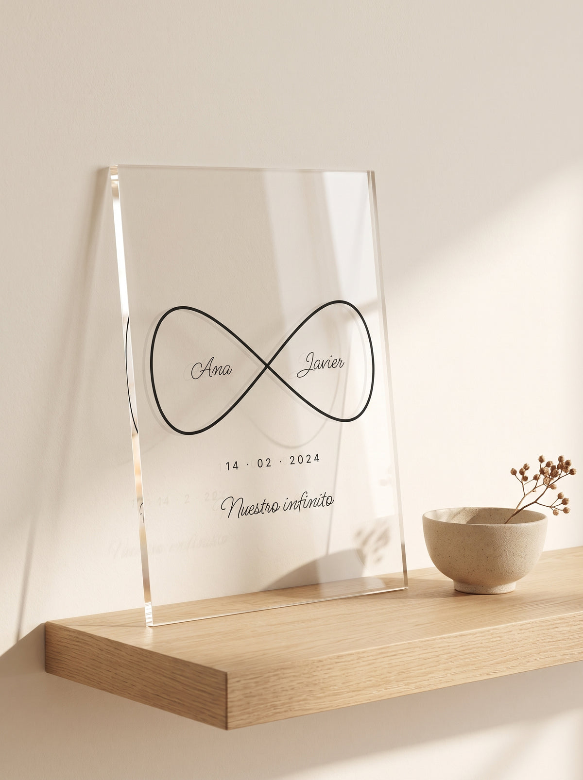 Placa de metacrilato personalizada infinito con nombres apoyada en una balda de roble junto a un cuenco de cerámica y una rama seca