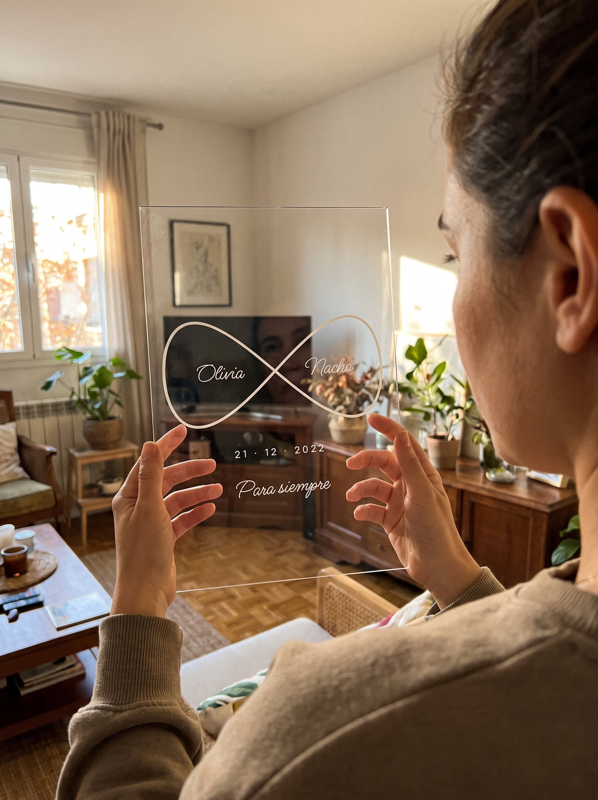 Sosteniendo la placa de metacrilato personalizada infinito con nombres a contraluz junto a una ventana