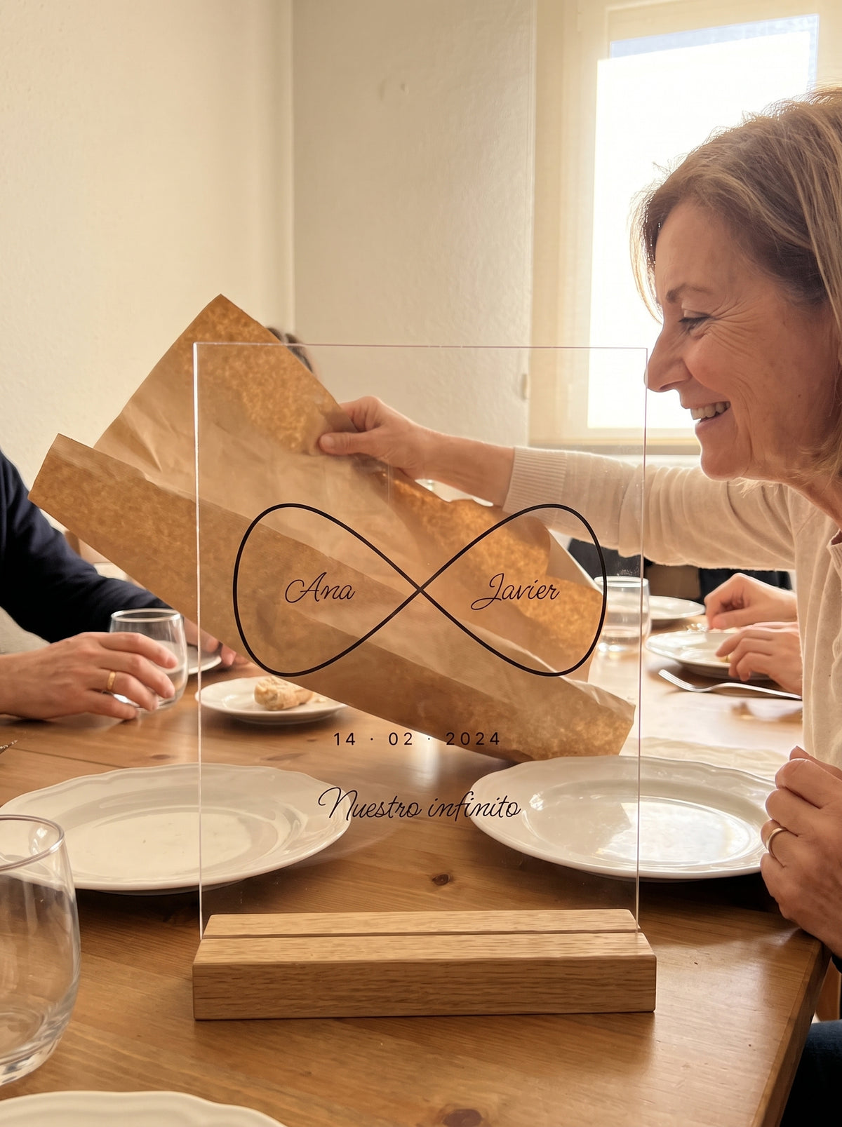 Abriendo el regalo de la placa de metacrilato personalizada infinito con nombres en una comida familiar