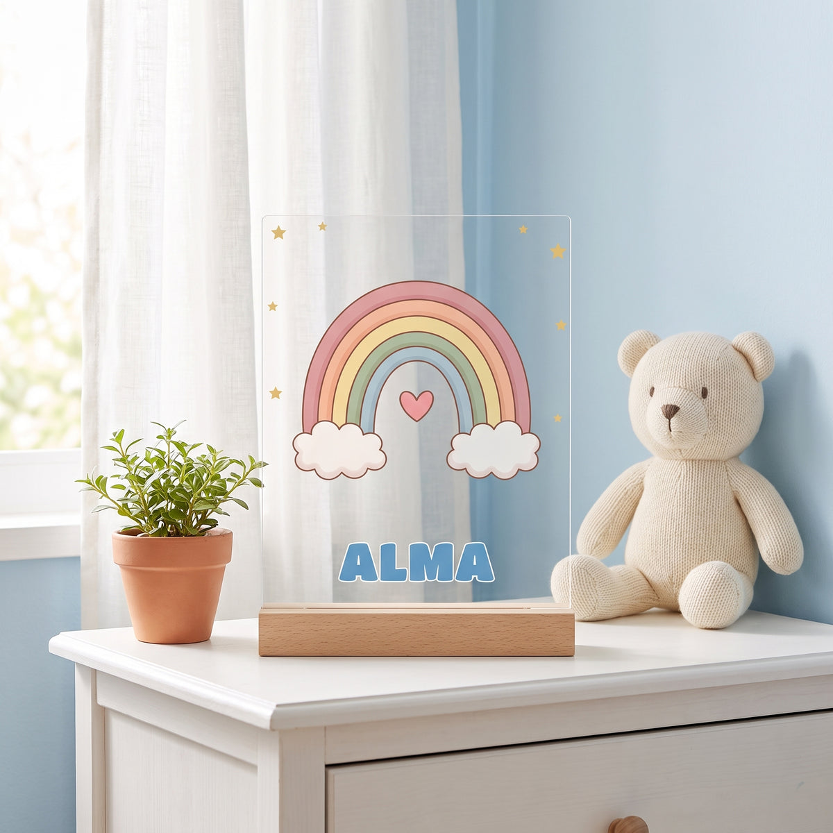 Lámpara infantil personalizada con nombre y dibujo del cielo con arcoíris y el nombre Alma, sobre una cómoda en un dormitorio infantil