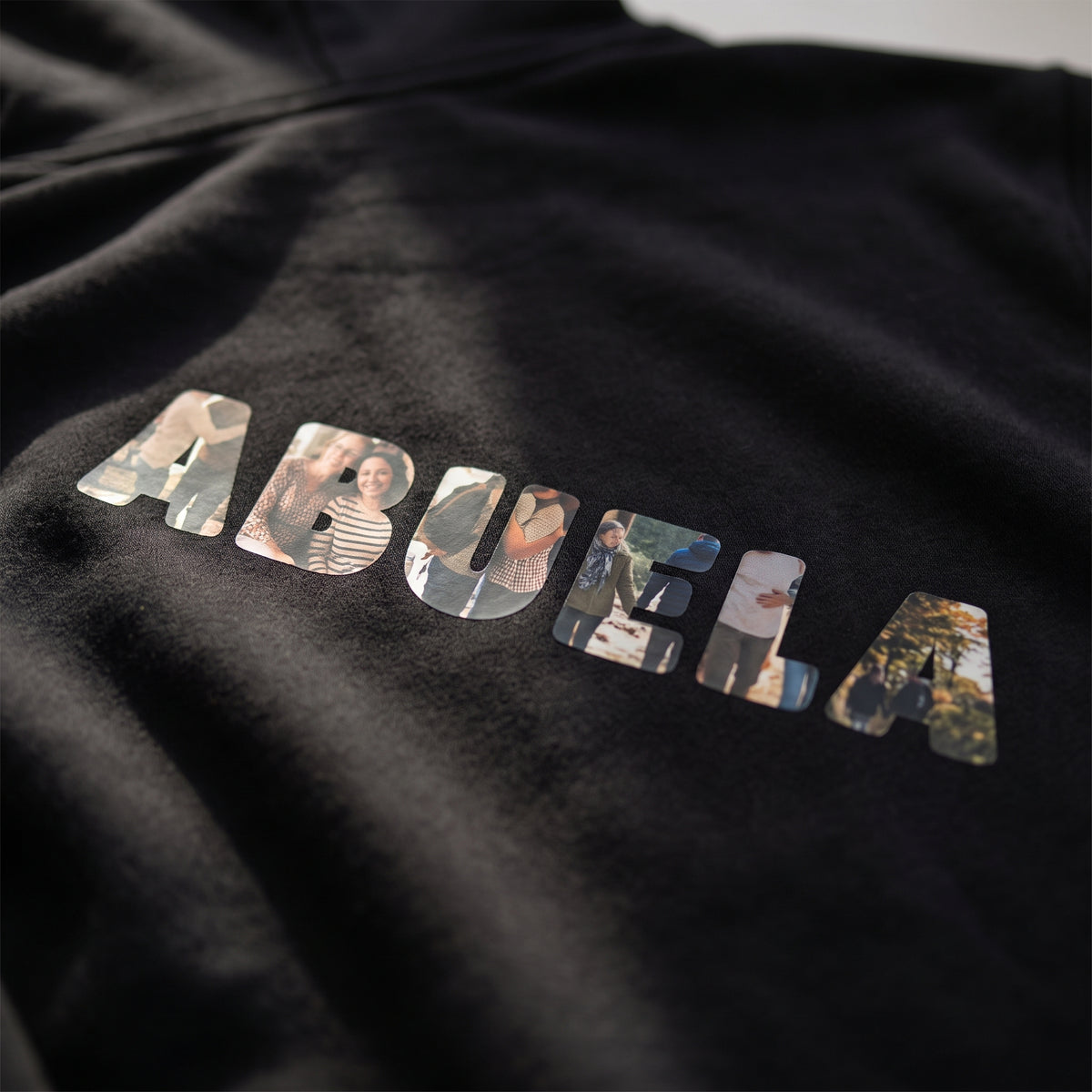 Detalle del estampado DTF de la palabra ABUELA con las letras rellenas de fotos sobre el tejido de una sudadera con capucha negra