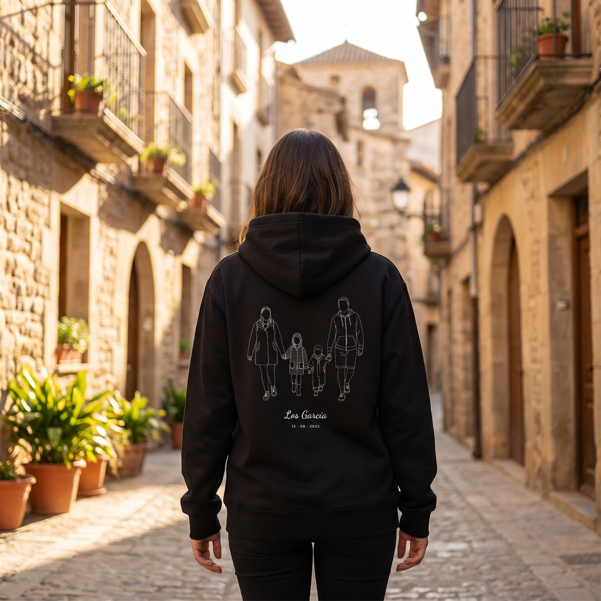 Mujer de espaldas con la sudadera con capucha negra personalizada con el dibujo lineal de una familia de cuatro y «Los García», estampado en la espalda