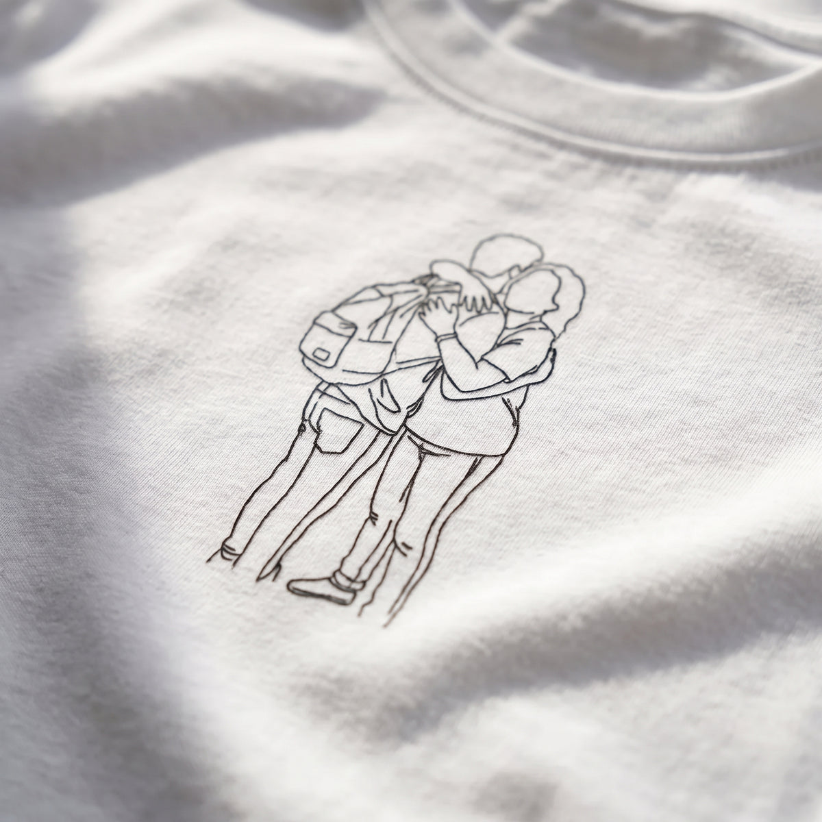 Detalle del estampado DTF del dibujo lineal de una pareja abrazada sobre el tejido de una camiseta blanca