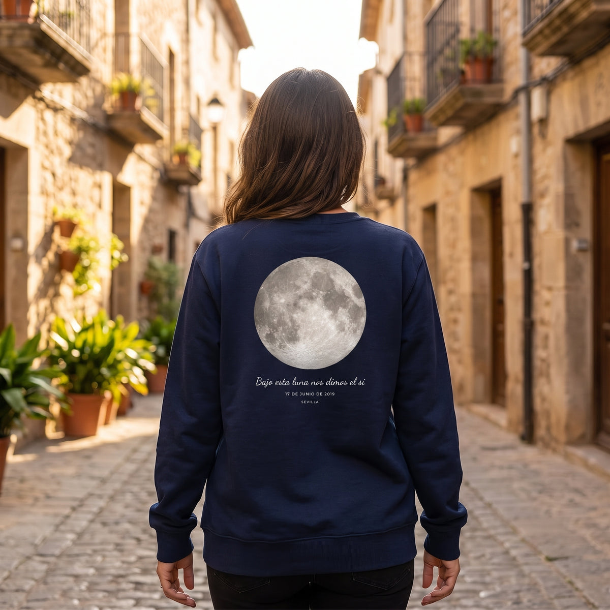 Mujer de espaldas con la sudadera azul marino personalizada con la luna de la noche elegida y «Bajo esta luna nos dimos el sí» estampado en la espalda