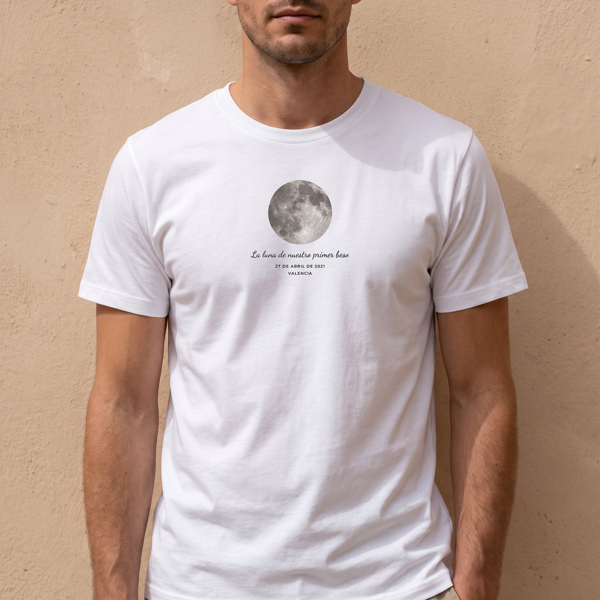 Hombre con la camiseta blanca personalizada con la luna de la noche elegida y «La luna de nuestro primer beso» estampado en el pecho