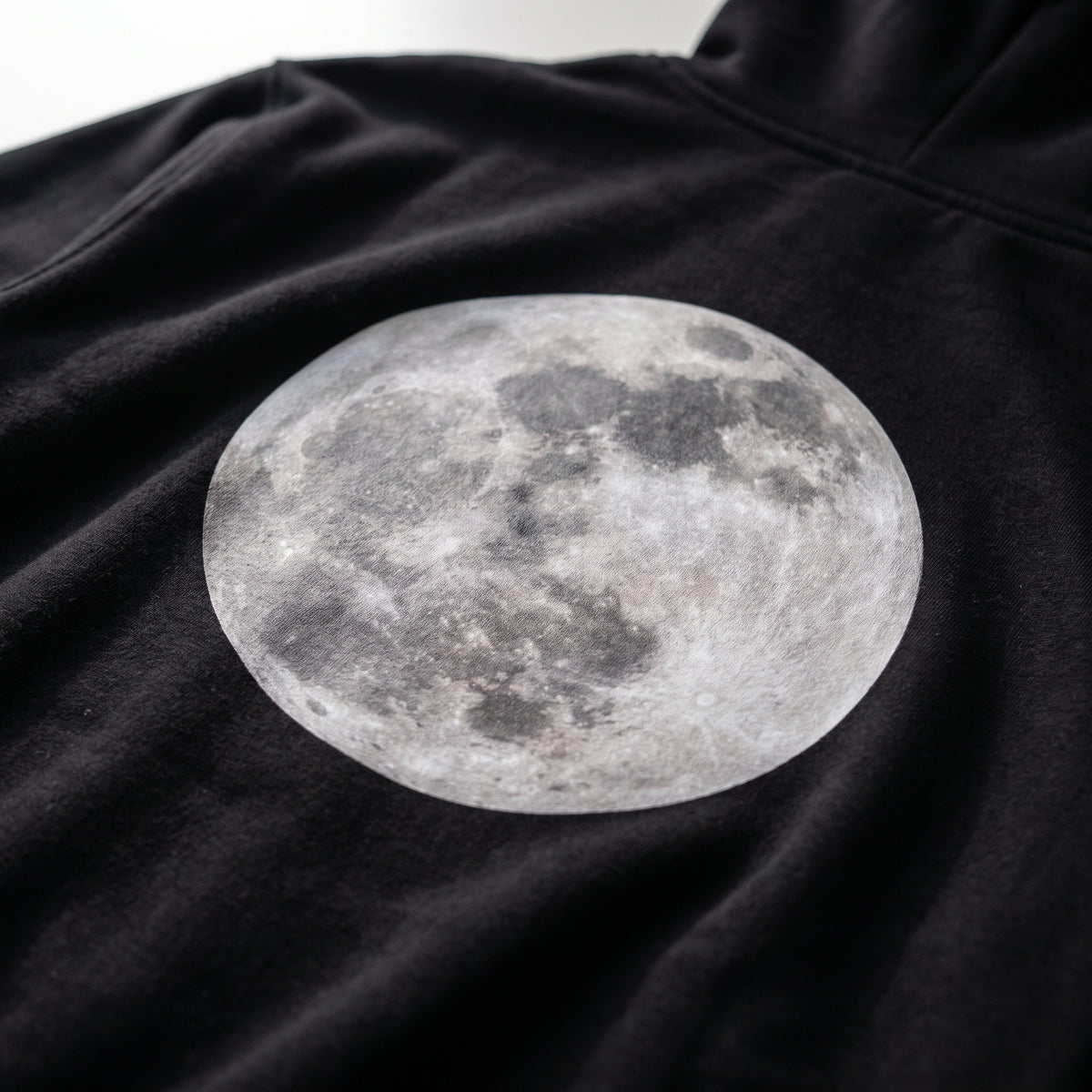 Detalle del estampado DTF de la luna de la noche elegida y «La luna de la noche en que nos conocimos» sobre el tejido de una sudadera con capucha negra