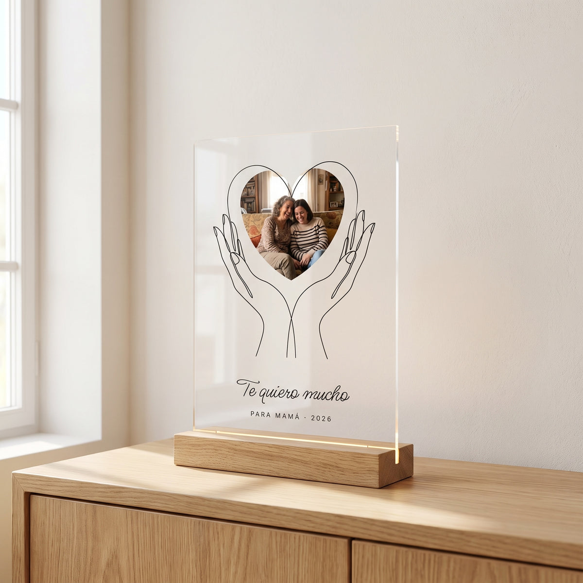 Placa de metacrilato personalizada con unas manos que sostienen la foto sobre un aparador de roble en una habitación luminosa, con su base de madera con luz