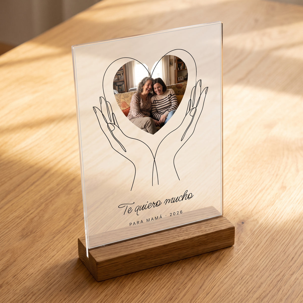Placa de metacrilato personalizada con unas manos que sostienen la foto encajada en su base de roble, con la luz apagada