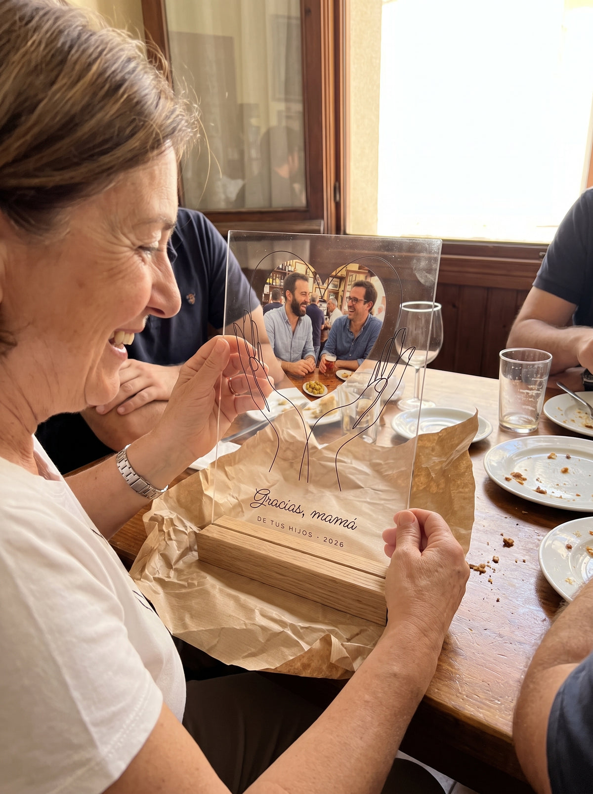 Abriendo el regalo de la placa de metacrilato personalizada con unas manos que sostienen la foto en una comida familiar