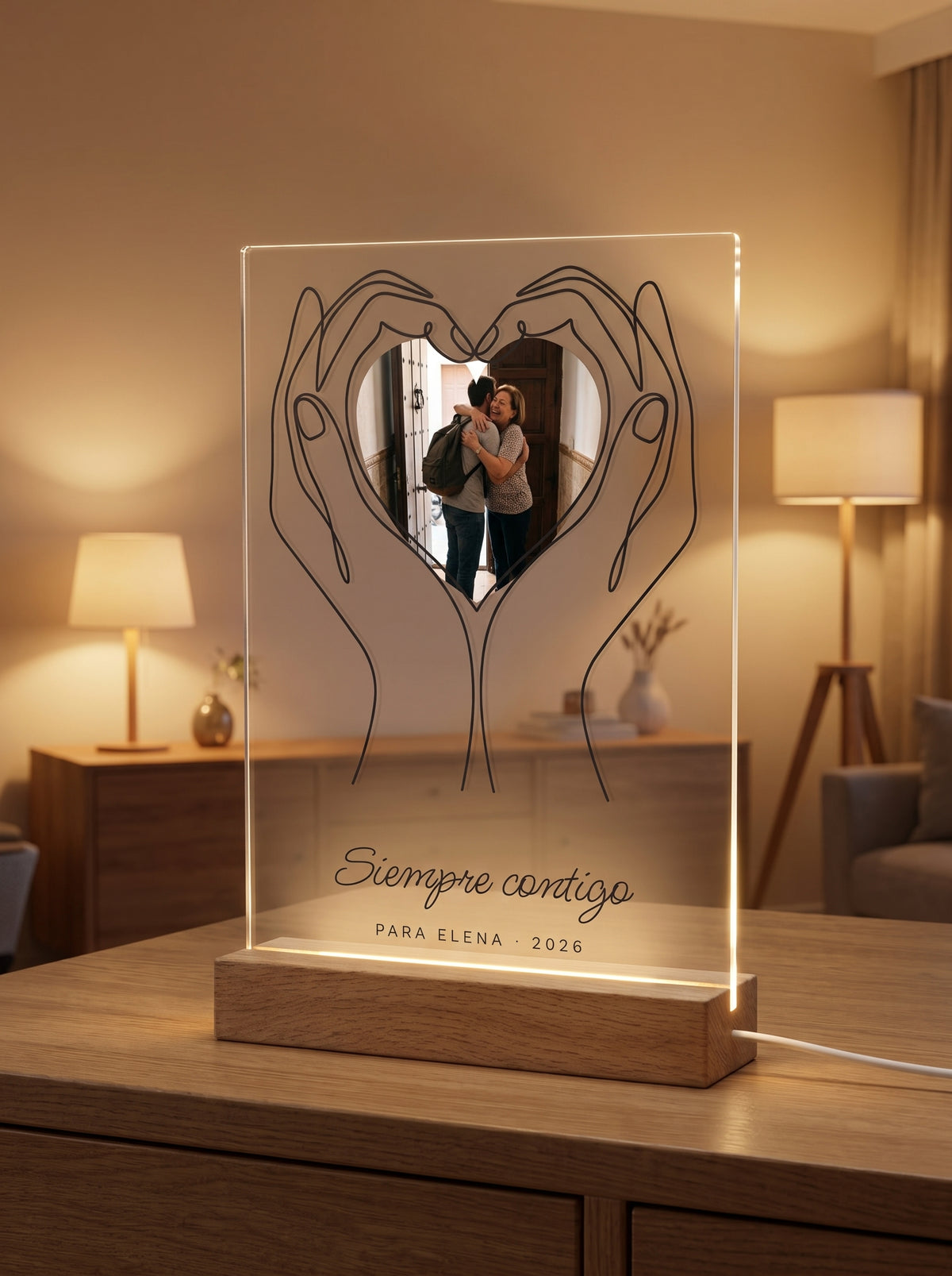 Placa de metacrilato personalizada con unas manos que sostienen la foto encendida sobre su base de roble con luz LED, en un salón al atardecer