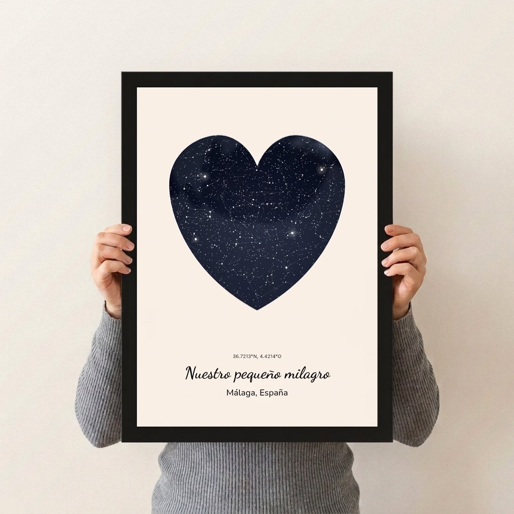 Cuadro mapa estelar de nacimiento con forma de corazón y marco negro sostenido con las manos