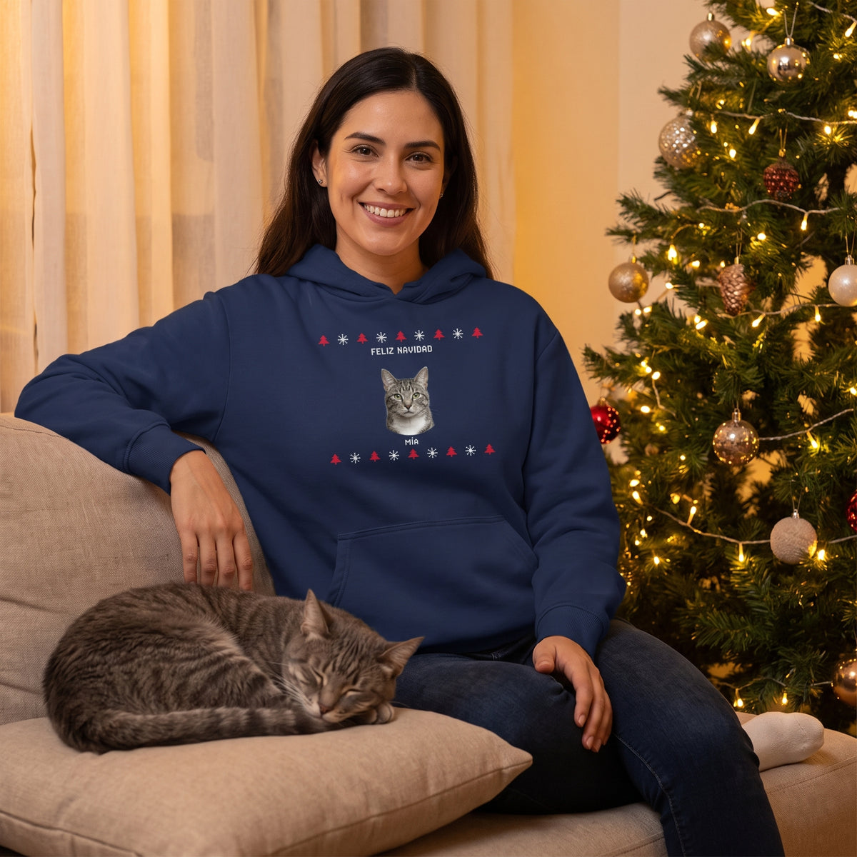 Mujer junto al árbol de Navidad con su gata, con la sudadera con capucha azul marino personalizada con la cara de la gata, Mía, en estilo jersey de punto navideño