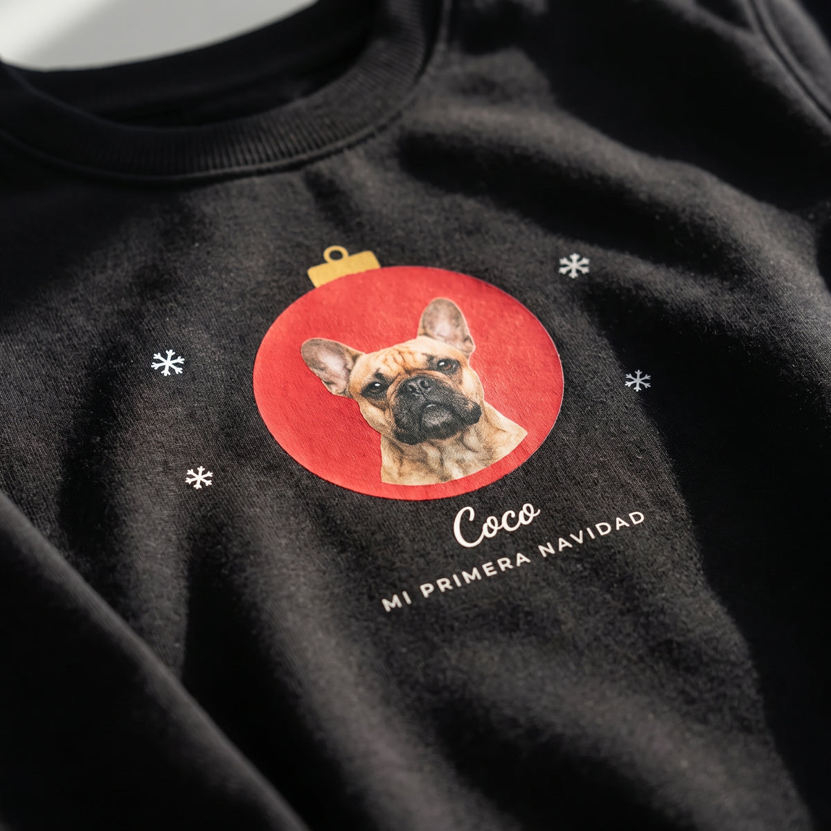 Detalle del estampado DTF de un bulldog francés dentro de una bola de Navidad roja, con el nombre Coco y «Mi primera Navidad», sobre una sudadera negra