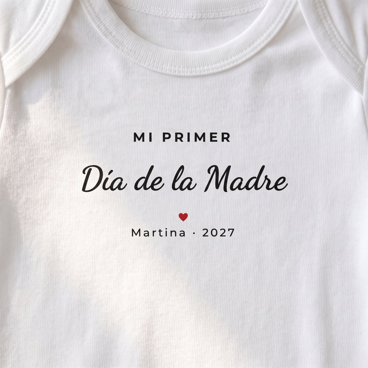 Detalle del estampado en el body: «MI PRIMER Día de la Madre», un corazón rojo y «Martina · 2027»