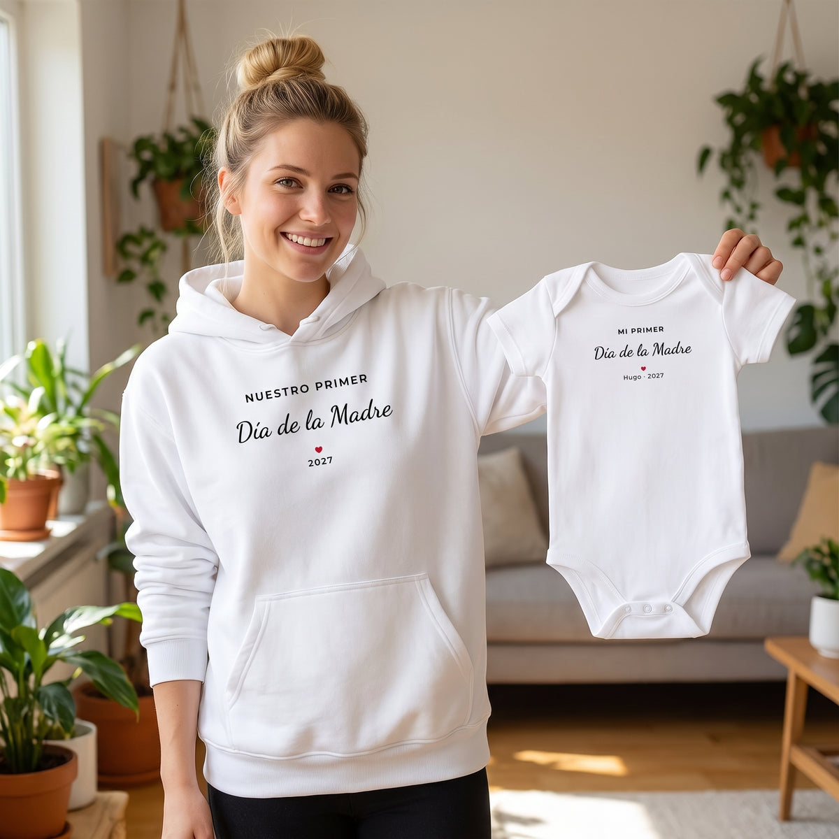 Mamá con sudadera con capucha «NUESTRO PRIMER Día de la Madre 2027» enseñando el body a juego «MI PRIMER Día de la Madre · Hugo · 2027»