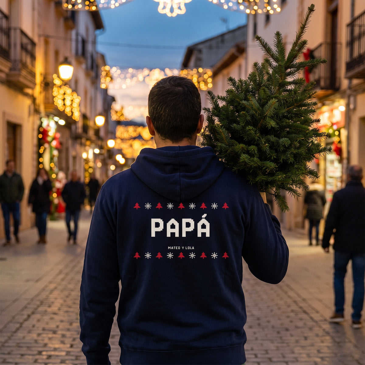 Padre de espaldas llevando un árbol de Navidad con la sudadera con capucha azul marino personalizada con PAPÁ en estilo jersey de punto navideño en la espalda
