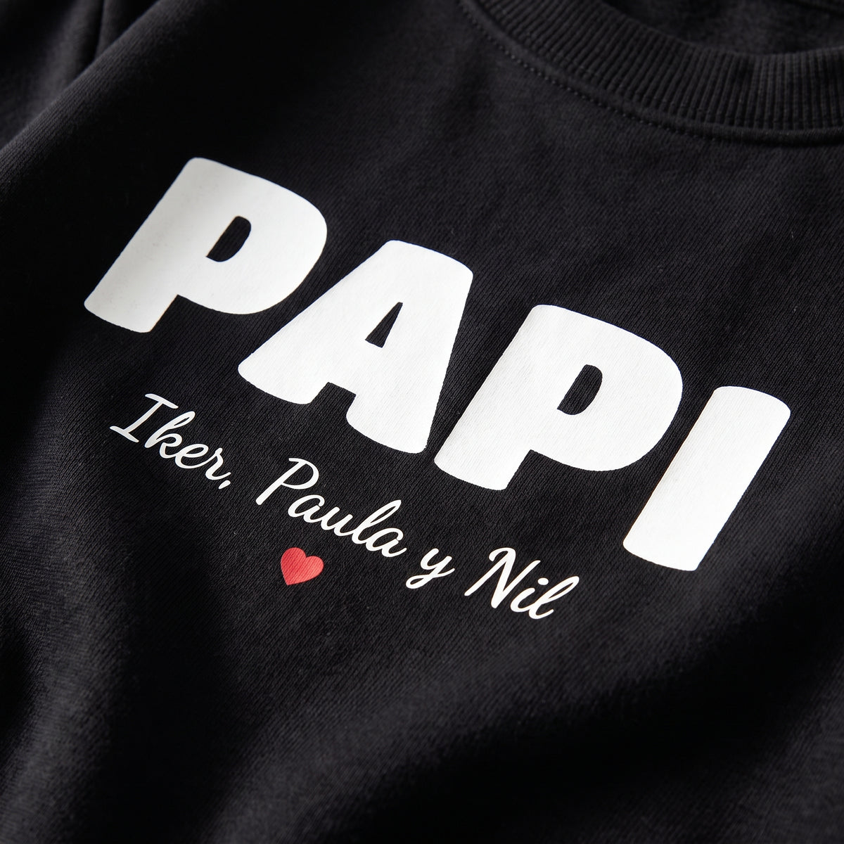 Detalle del estampado DTF de PAPI en letra retro con los nombres de sus hijos y un corazón rojo sobre una sudadera negra