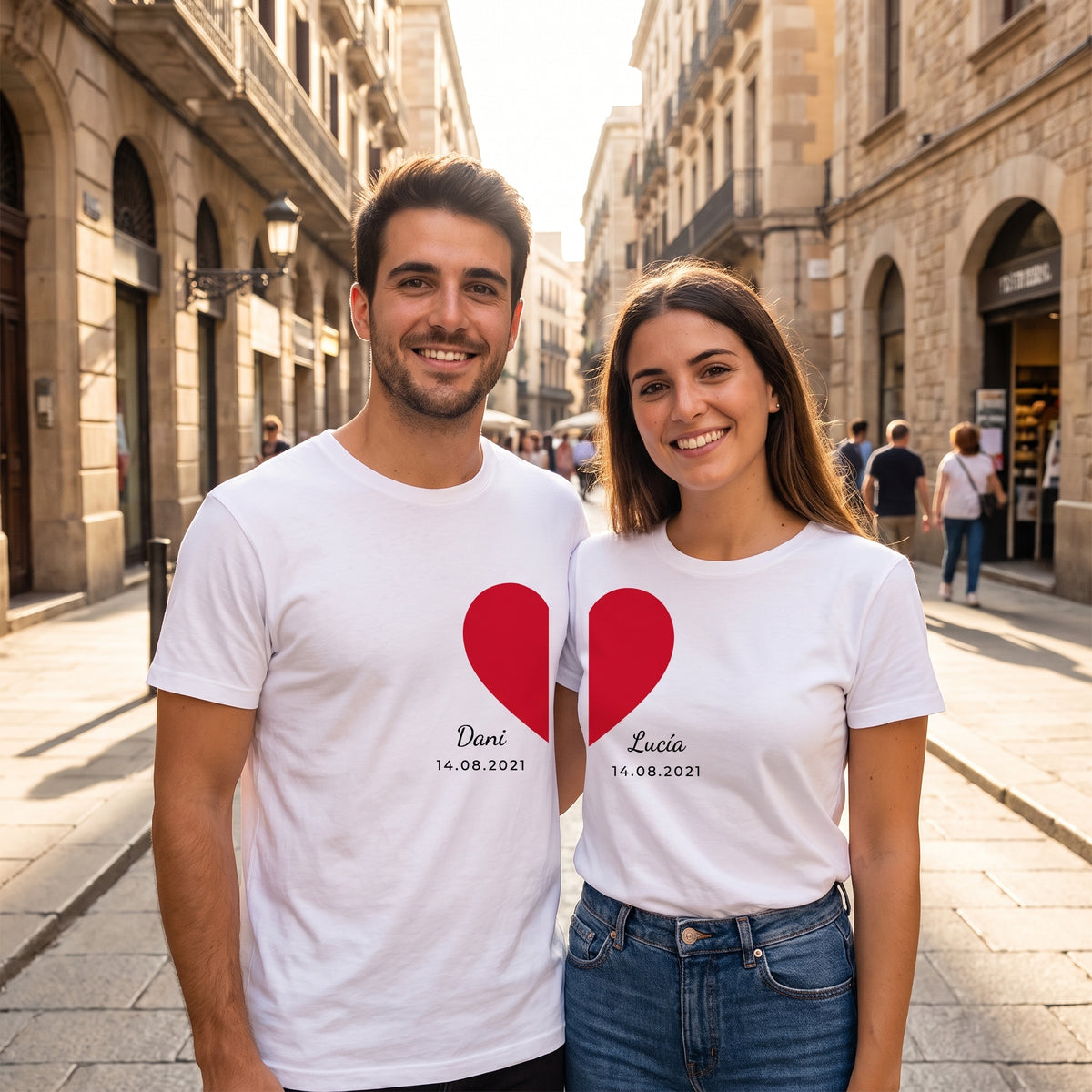 Pareja sonriendo en la calle con camisetas blancas a juego: cada una lleva medio corazón rojo que se completa al ponerse juntos, con «Dani», «Lucía» y 14.08.2021