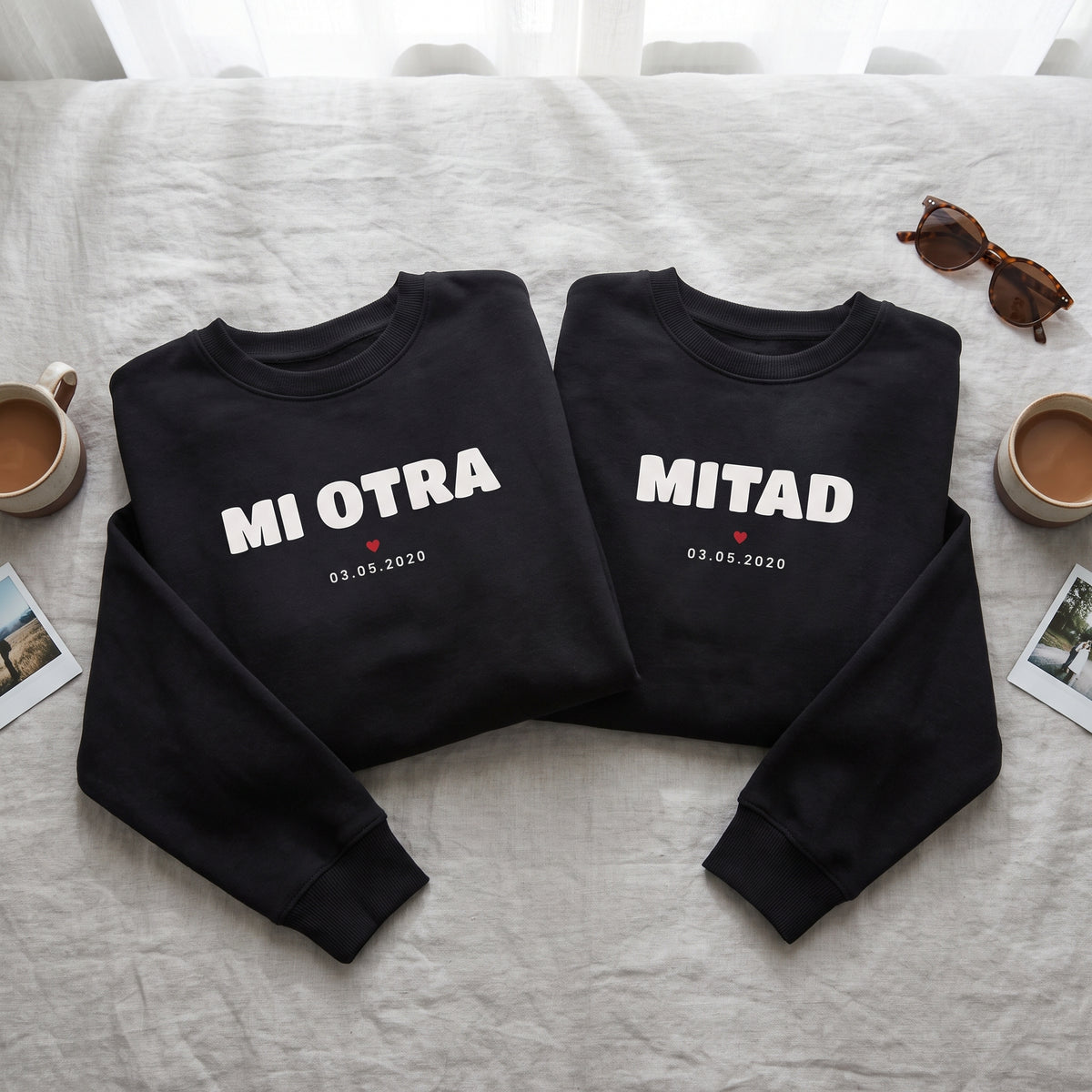 Dos sudaderas negras a juego sobre la cama: «MI OTRA» en una y «MITAD» en la otra, con un corazón rojo y la fecha 03.05.2020