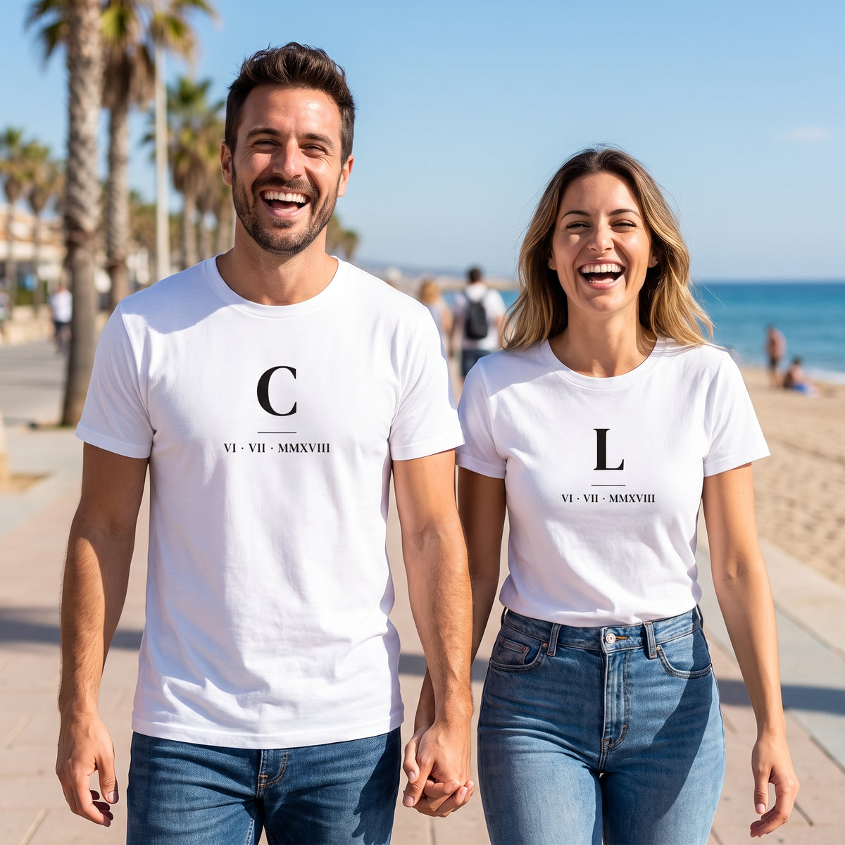 Pareja paseando de la mano por el paseo marítimo con camisetas blancas a juego: «C» y «L» con la fecha en números romanos VI · VII · MMXVIII