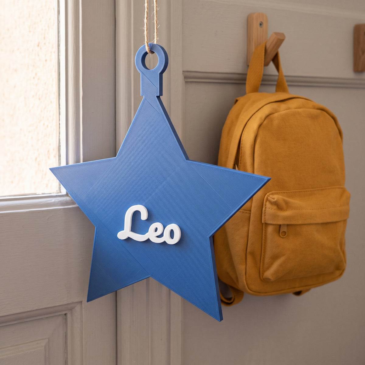 Placa de puerta en forma de estrella azul con el nombre Leo junto a una mochila infantil