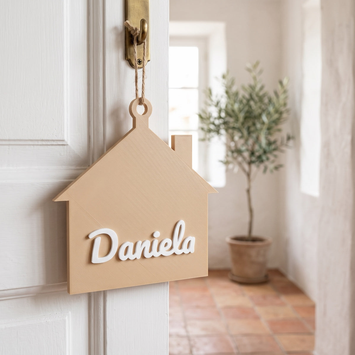 Placa de puerta en forma de casita con el nombre Daniela colgada en una puerta blanca