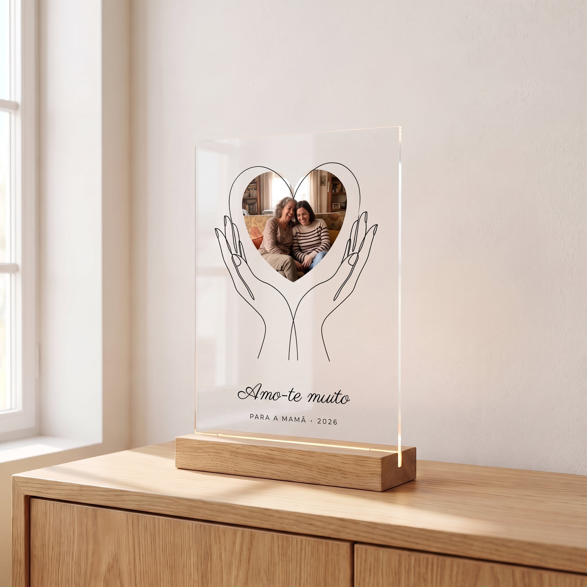 Placa de metacrilato personalizada con unas manos que sostienen la foto sobre un aparador de roble en una habitación luminosa, con su base de madera con luz