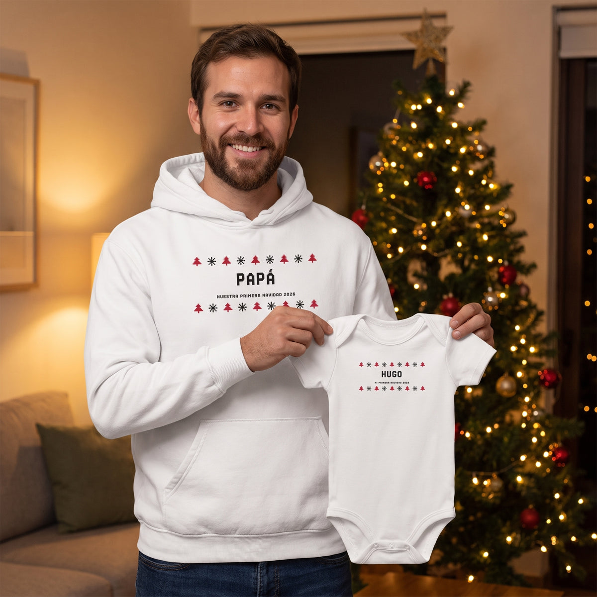 Papá junto al árbol de Navidad con la sudadera con capucha «PAPÁ · NUESTRA PRIMERA NAVIDAD 2026», estilo jersey de punto, enseñando el body a juego «HUGO»