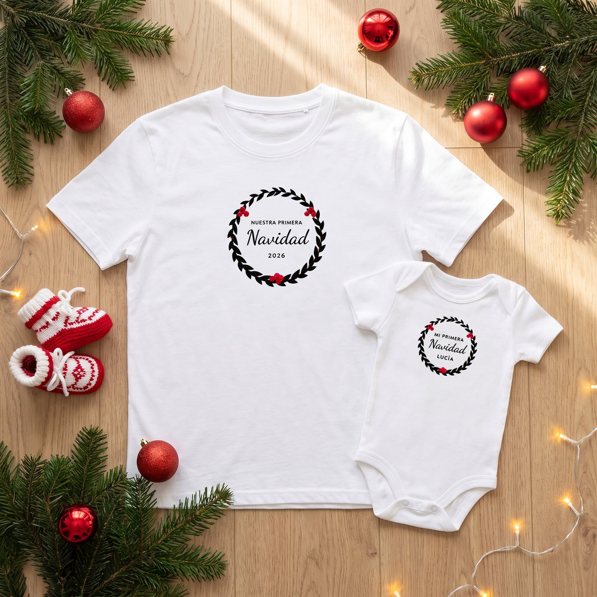 Camiseta y body blancos con la corona de hojas y bayas «NUESTRA PRIMERA Navidad 2026» y «MI PRIMERA Navidad · LUCÍA», con ramas de pino y patucos